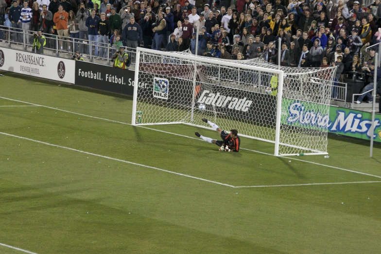 the soccer player has his leg on the ground while the soccer goalie dives over to block it