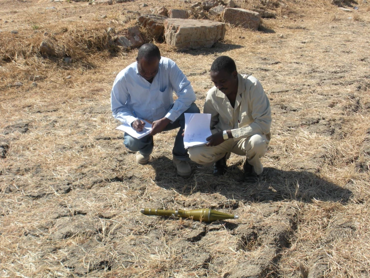 two men are on a dry field with plants