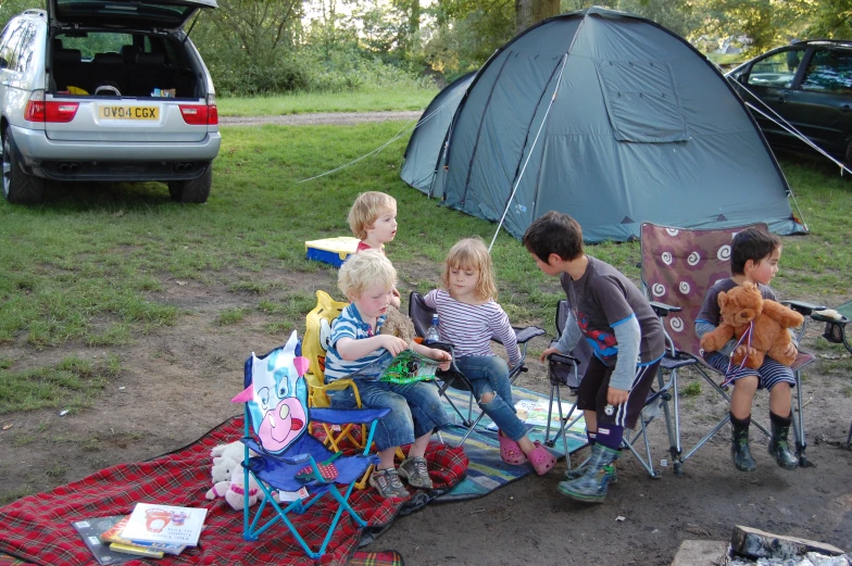 some children with a teddy bear near a tent