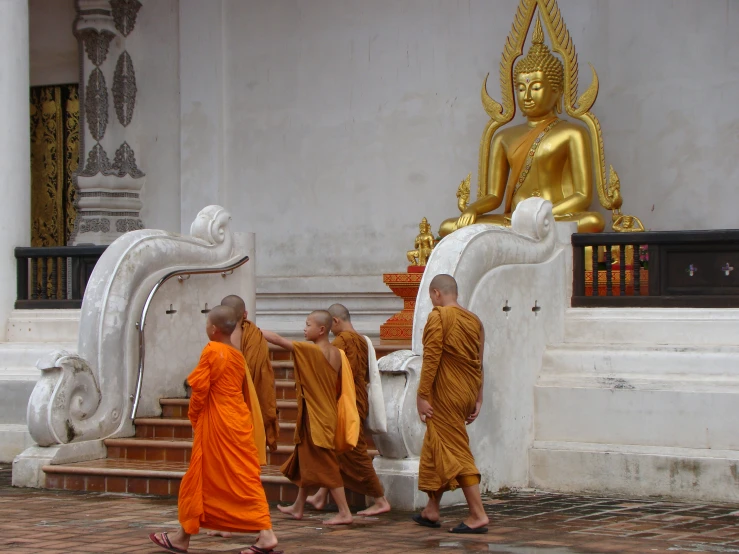 three monks walking outside towards a golden buddha