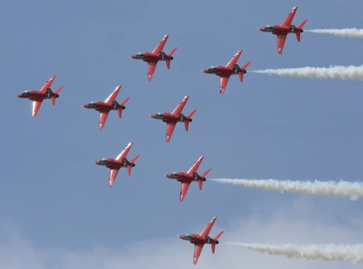 nine red jets flying in formation with smoke trailing behind them