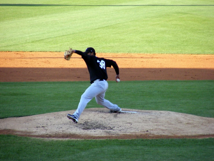 a man in white pants and black shirt is throwing a baseball