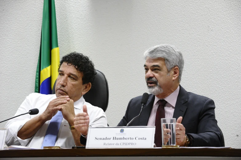 two men sitting at a desk with two signs and microphones in front of them