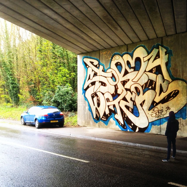 a car parked under an overpass with graffiti on it