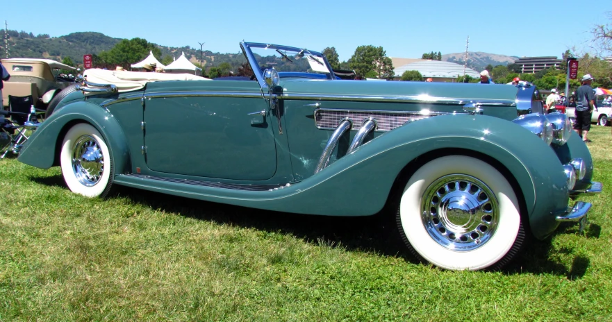 an old car parked on some grass next to people