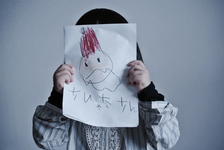 a girl holds up a paper with a drawing on it