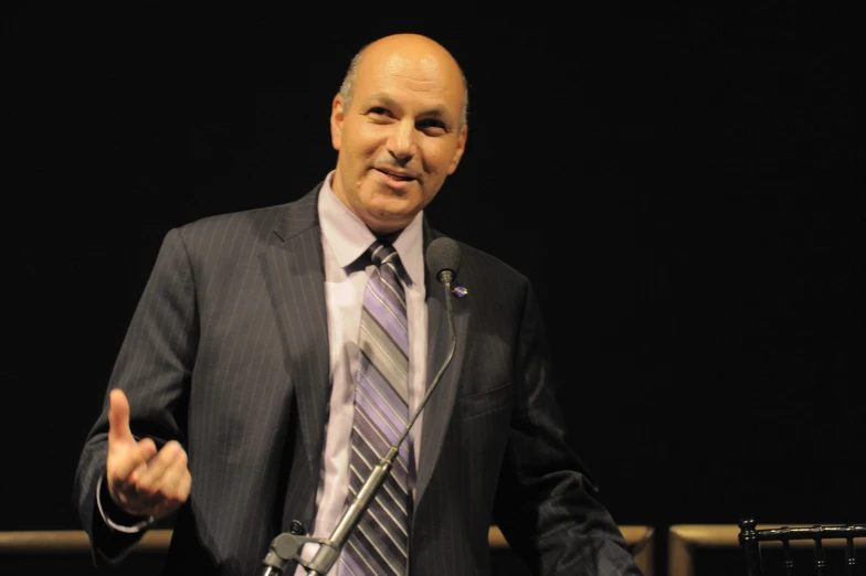 a man giving a speech on stage with a microphone in front of him