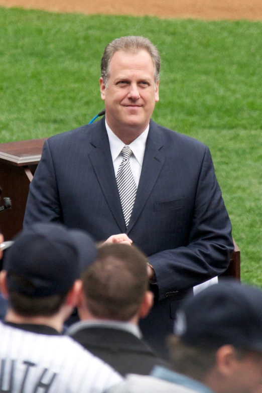 a man in a suit and tie standing near a bench with other men at a baseball game