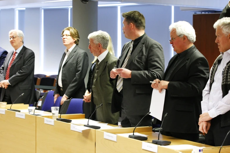 the group of people who are wearing suits and ties standing behind wooden tables