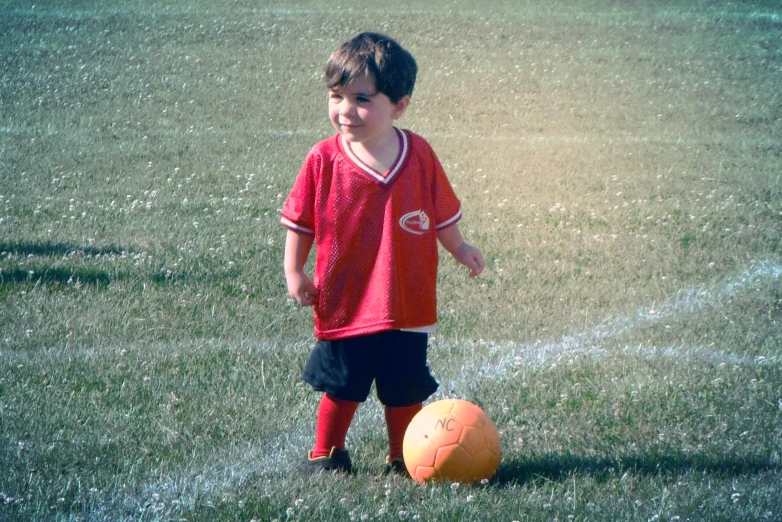 a little boy in red shirt next to a yellow soccer ball