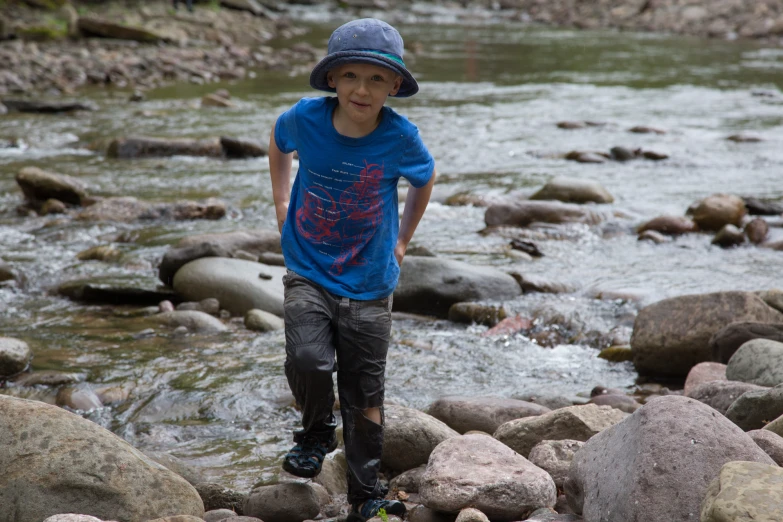 a boy wearing a hat walking along rocks