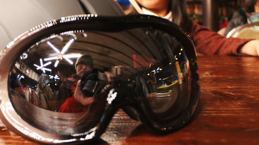 a mirrored image shows people standing and sitting behind a shiny metal mirror