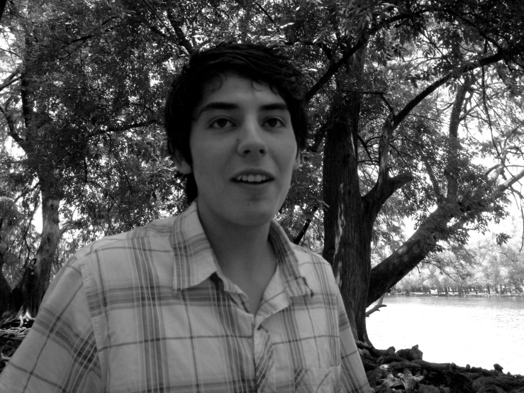 a young man standing under a tree by the water