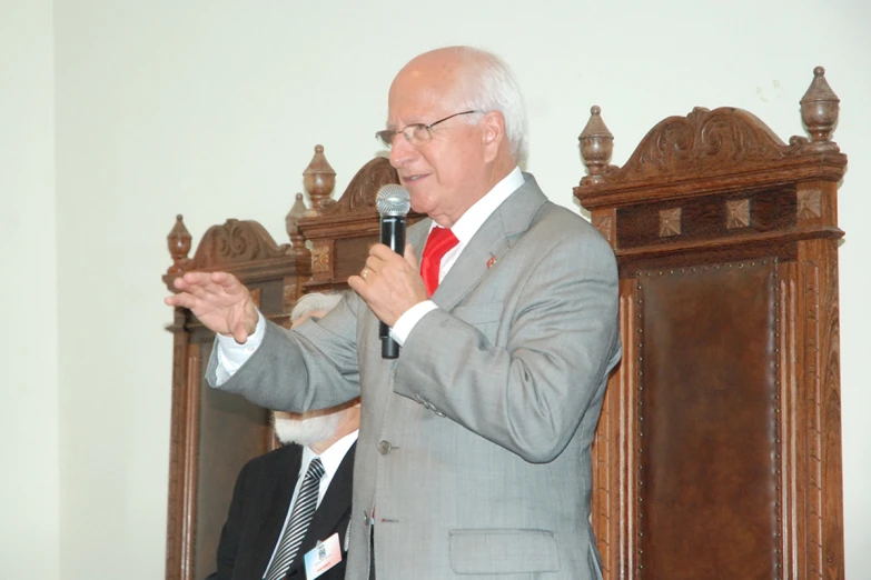 an older man in grey suit and tie standing next to a microphone