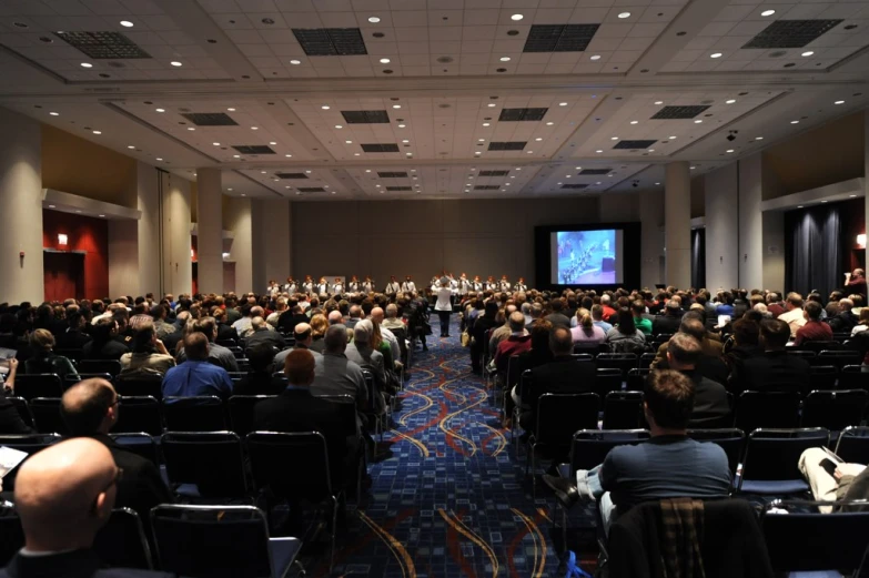 an auditorium with rows of people sitting in it and a projection screen