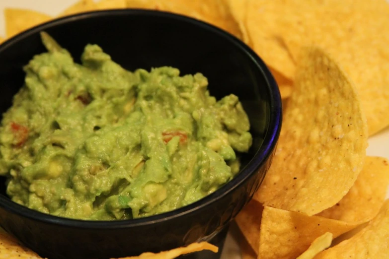 guacamole is in a bowl next to tortilla chips