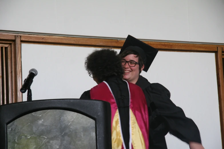 the graduate smiles as he hugs a woman