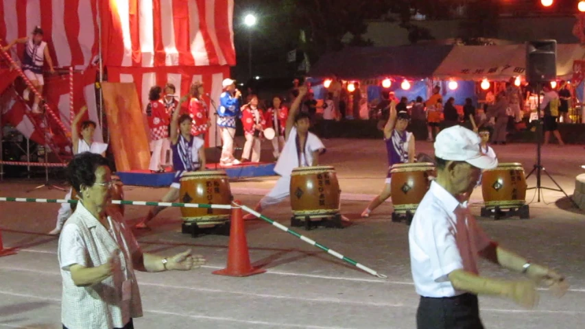 a man and woman performing on drums with people standing around in the background