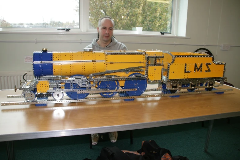 a man standing next to a model train on a table