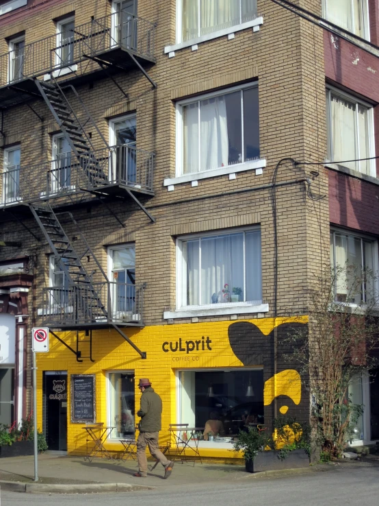 a man walking down a street past a very tall yellow building