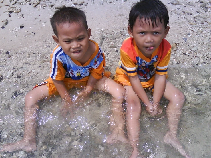 two children sit in the water with each other