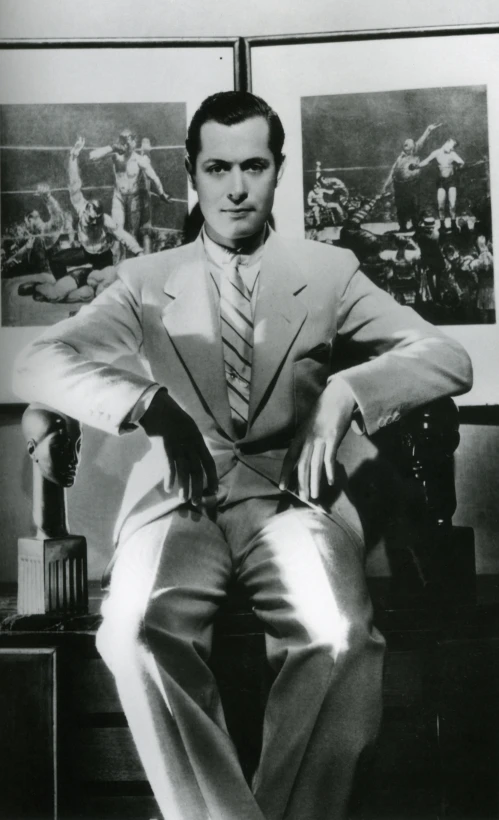 man in suit sitting down with hat and glove on