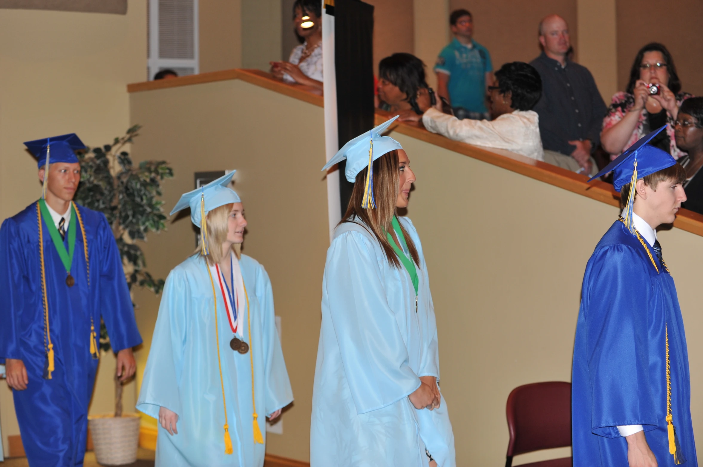 people stand in the audience and watch as one man adjusts his cap and gown