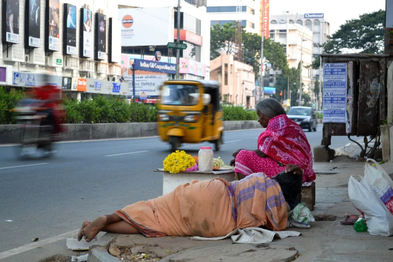 two women sitting at a side walk next to a street