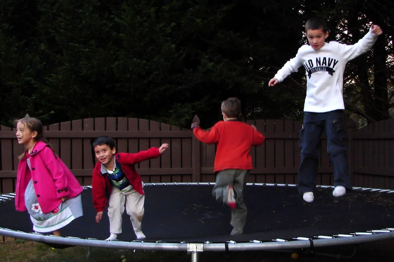 three children playing on an outdoor trampoline with trees in the background