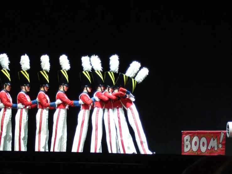 a line of people are dressed in long red jackets and white pants