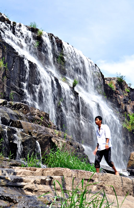 a man standing in front of a waterfall in the mountains