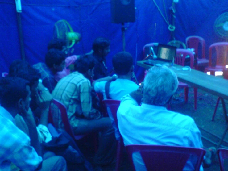 several people seated at tables in front of blue screen with a light on them