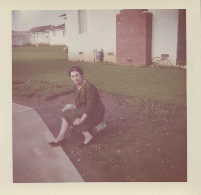 an old pograph of a woman sitting on the curb outside a house