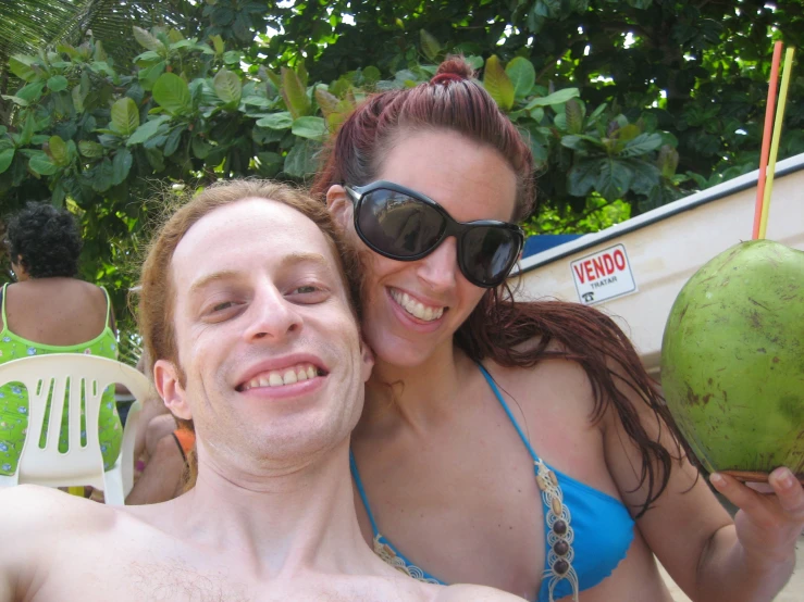 a woman and man in sunglasses are next to a coconut