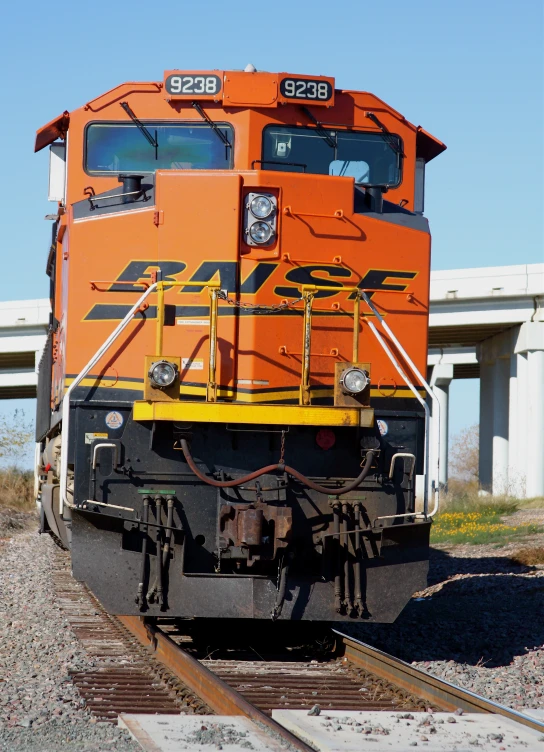 an orange train sitting on the tracks by some buildings