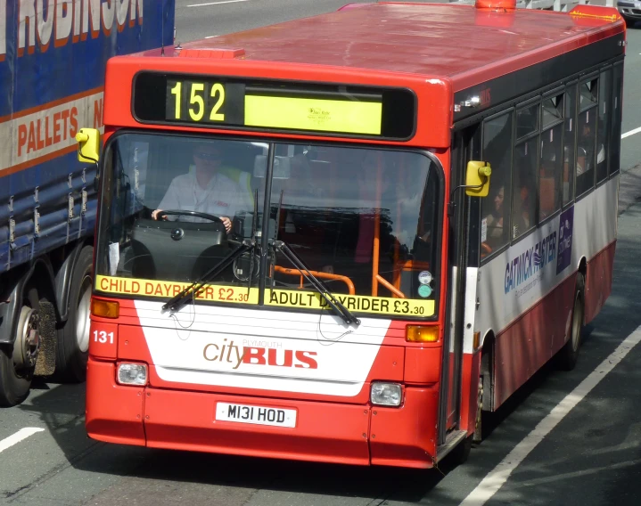 a red city bus on the road near a truck
