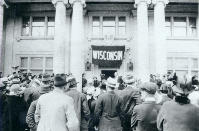 men in suits stand at the entrance of a building with an inscription on it