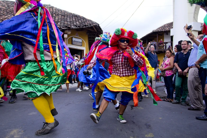 a group of people dance down the road in colorful costumes