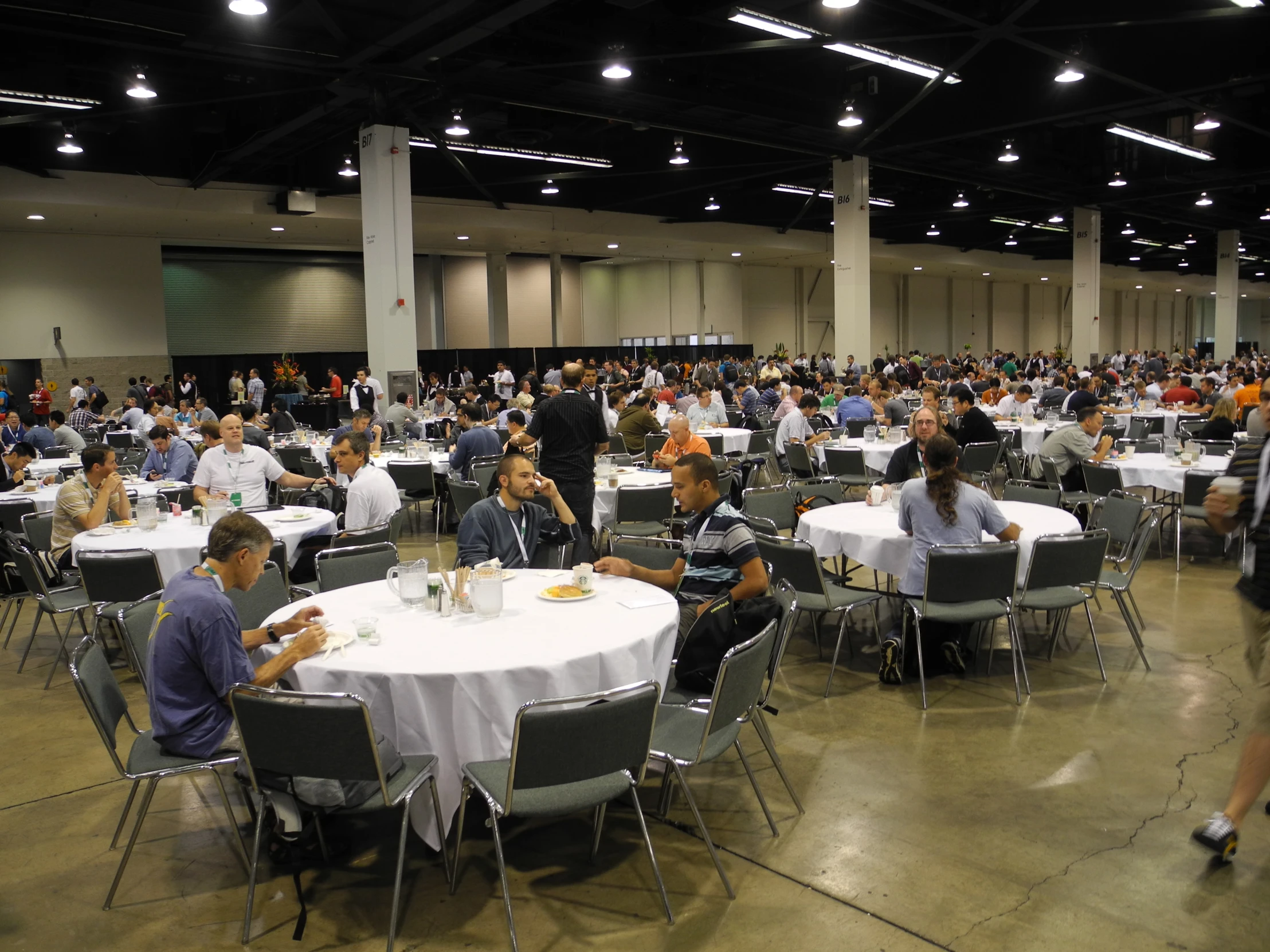 a gathering of people sitting at tables in an indoor convention hall