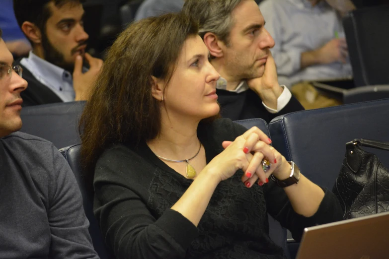 a woman sitting in a blue theater, with her hand folded in front of her face and on the lap