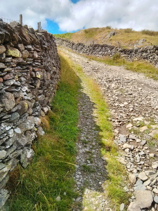 a dirt road leading to a stone wall and grassy field