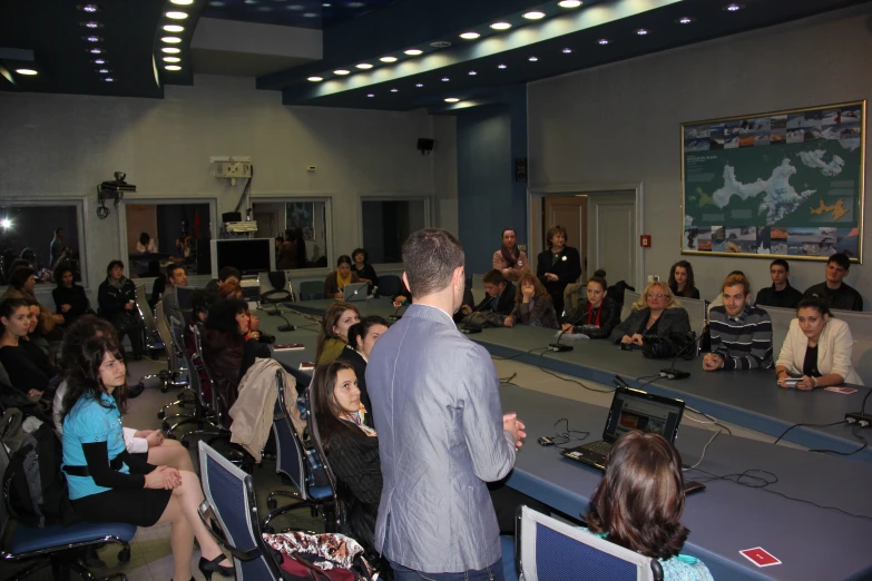 people sit in chairs around a boardroom and listen to a speaker