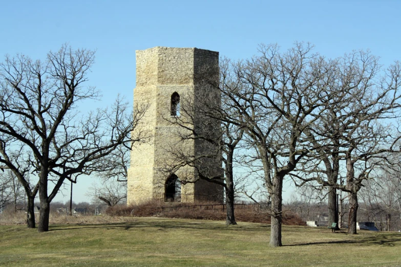 a stone tower is between several trees and the grass