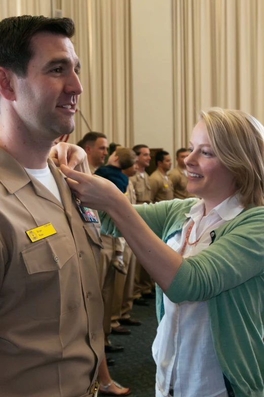 the man is adjusting the woman's collar on her uniform