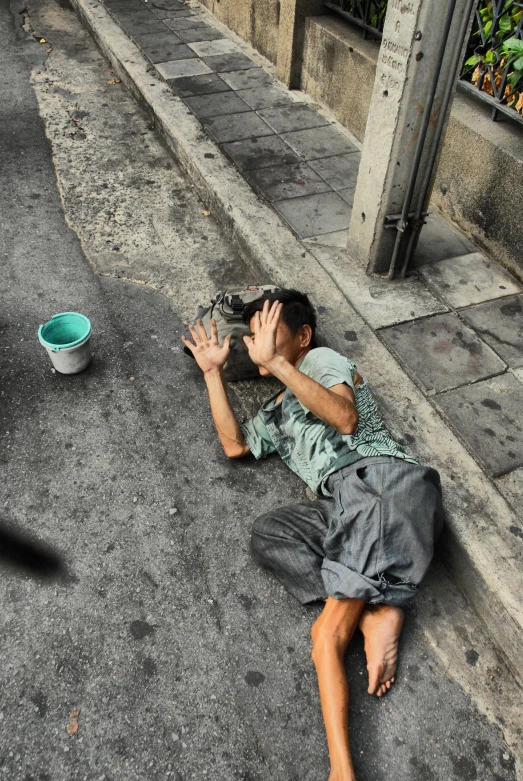 a man is sleeping on the sidewalk and holding his hand to his face