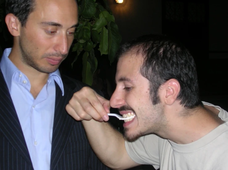 a man brushing his teeth with another person in the background