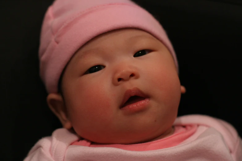 a small baby in pink sitting down wearing a pink hat