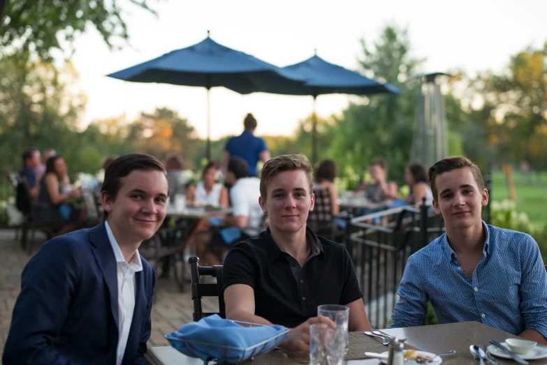 three people sitting down for dinner at the outdoor table