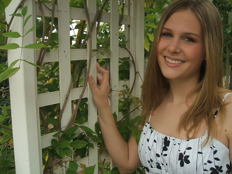 a young lady posing in front of an outdoor trellis