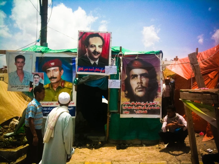 a man wearing a turban sits next to his tent where posters are hung